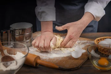 Foto op Canvas Women's hands, flour and dough. A woman in an apron cooking dough for homemade baking, a rustic home cozy atmosphere, a dark background with unusual lighting. © Volodymyr