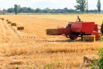 Fototapeta premium Rectangular baler discharges a straw bale in a field during the harvesting process