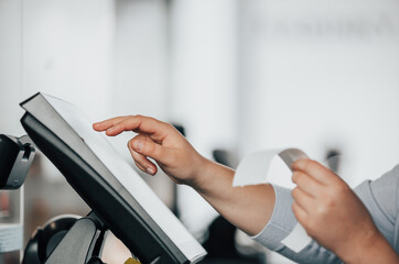 Young saleswoman doing process payment on touchscreen POS, counting sale in the cash register,...