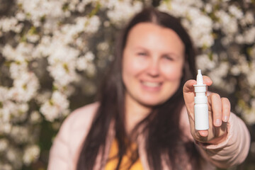 Allergy concept, young woman with nose or nasal spray in hand in front of blooming a tree during spring season, healthcare