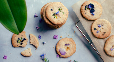 Delicious homemade biscuits with edible flowers on a blue background on table in a kitchen. Food decorated spring flowers for breakfast. Close up. Panoramic.