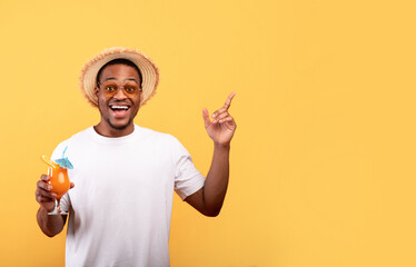 Amazing offer. Excited African American man with yummy summer cocktail pointing at blank space on yellow background
