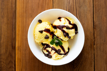Vanilla ice cream scoops sundae in bowl with chocolate syrop on wooden background, copy space