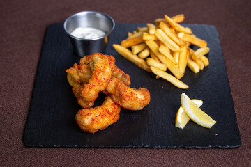 fish in batter with sauce and fries on a black plate