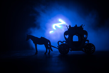 Little carriage with horse miniature on table. Creative decoration on dark toned foggy background.