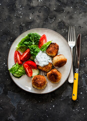 Fresh kale, tomato salad and canned tuna potato fish balls with greek yogurt cilantro sauce on dark background, top view