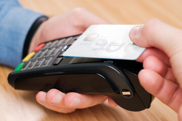 Close up man hand paying with contactless credit card with NFC technology using wireless payment terminal. Cashless payment during pandemic of coronavirus 