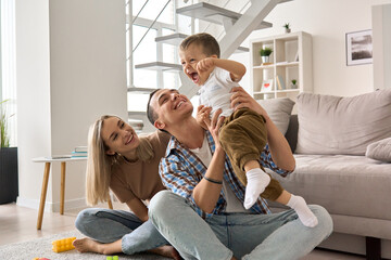Happy young family couple having fun playing with cute small toddler kid son in modern living room...
