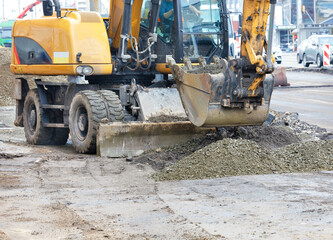 A heavy road excavator smooths a pile of rubble with a bucket at a construction site.