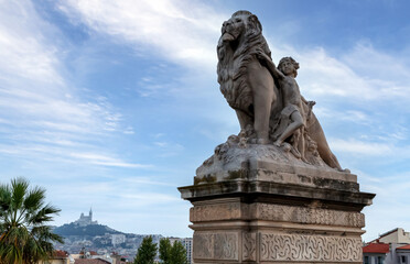 Fototapeta na wymiar A statue of the lion and child, historical monument in front of Saint-Charles station in Marseille, Notre-Dame de la Garde basilica in the background. Marseille, France.