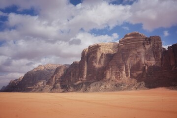 Fototapeta premium beautiful red relief weathered mountains in the Wadi Rum desert, beautiful white clouds in the blue sky, sunny day, contrasting shadows are on the mountains, nature of Jordan