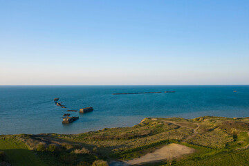 Fototapeta premium Le port artificiel de Arromanches au milieu de la mer de la Manche au pied d'une falaise en France, en Normandie, dans le Calvados, au bord de la Manche sous le Soleil.