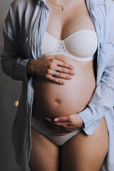 A pregnant girl holds her belly with her hands in lingerie. Pregnancy photo. 
