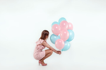 Fototapeta na wymiar A beautiful young girl sits with blue and pink balloons on a white background. Happiness, spring, holiday.
