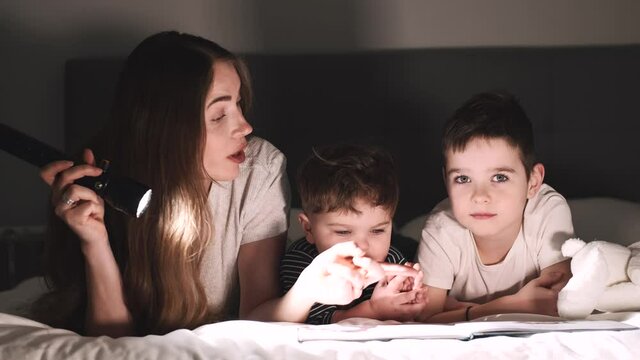 Mother reading scare story with sons under the sheet