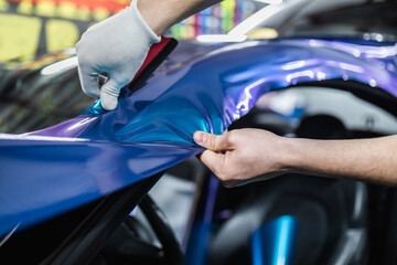 Car wrapping specialist putting vinyl foil or film on car. Selective focus.