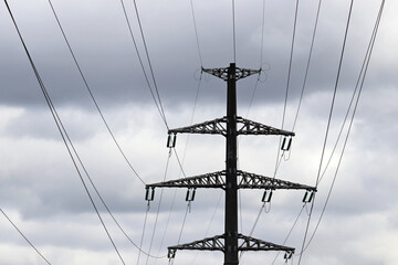 High voltage tower silhouette with electrical wires on storm sky background with dark clouds. Electricity transmission lines, power supply concept