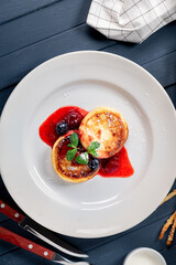 Cottage cheese pancakes on a white plate with sour cream and berry jam. Homemade breakfast, top view
