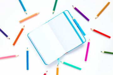 open blue notepad on a white background with place for text. pencils are scattered around the notebook.