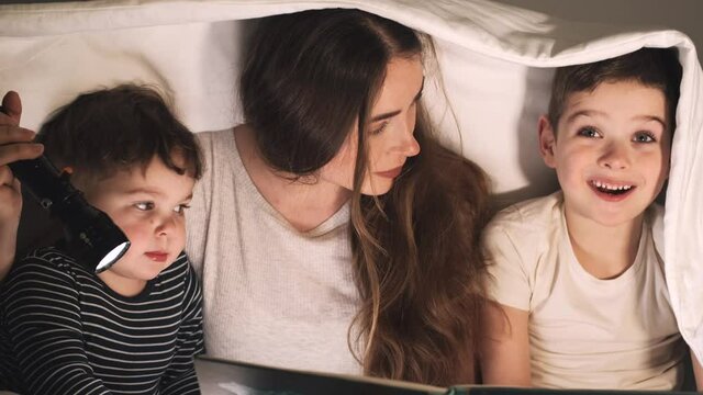 Mother reading scare story with sons under the sheet