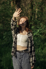 A girl stands under the rays of the sun in a nature photo. The girl covers herself with her hands from the sun. Bask in the sun