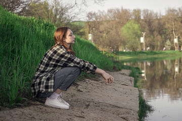 Portrait of a young girl on the background of the lake. The girl is sitting on the shore of the lake. Girl with red hair