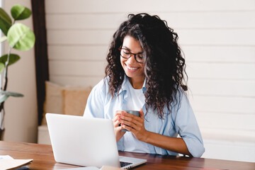 Cheerful relaxed young afro businesswoman having coffee break at work. African girl student elearning distance training course study work at home office. young,  watching online education webinar.