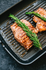Grilled buffalo beef steak with rosemary in black grill pan on the table, close-up.