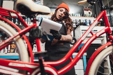 Fototapeta na wymiar Beautiful young female mechanic talking on phone while repairing bicycles in a workshop..