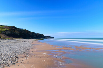La plage de sable et de galets au pied des falaises de Omaha beach en France, en Normandie, dans le Calvados, au bord de la Manche. - obrazy, fototapety, plakaty