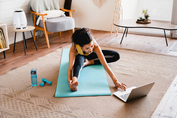 Young slim african girl stretching at home using laptop. Cheerful African woman stretching up In...