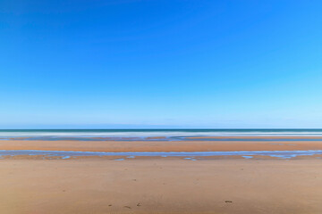 Fototapeta na wymiar La plage de sable de Omaha beach en France, en Normandie, dans le Calvados, au bord de la Manche sous le Soleil.