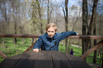 Fototapeta premium The boy sits at a wooden table in a cafe and makes various gestures with his hands