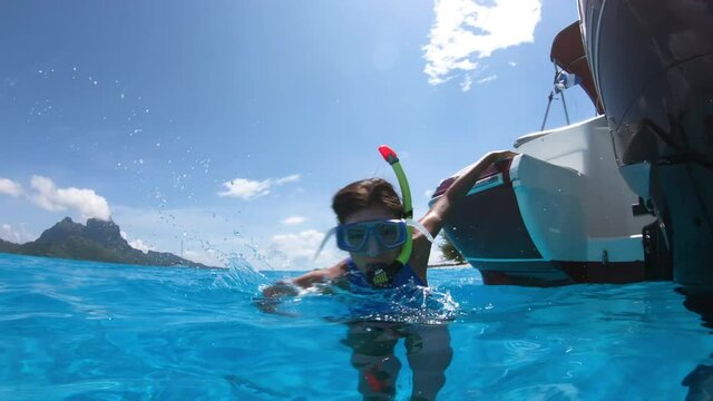 Snorkeling from boat in Bora Bora, Tahiti, French Polynesia. Woman jumping in crystal clear water with snorkel gear in coral reef lagoon with Bora Bora landmark Mount Otemanu in background