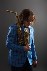Half-length studio portrait of a young musician guy holding a saxophone.
