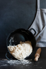 Dough in a black cast iron pan, rolling pin, gray apron in the background.