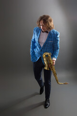 Fototapeta premium Full-length studio portrait of a young musician guy holding a saxophone.