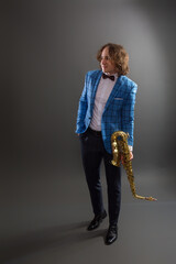 Full-length studio portrait of a young musician guy holding a saxophone.