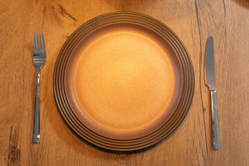 Empty brown plate with knife and fork on rustic wooden table copy space for text
