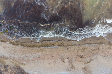 Steep sea shore and surf. Sea water muddy with sand after storm and algae. Aerial view.