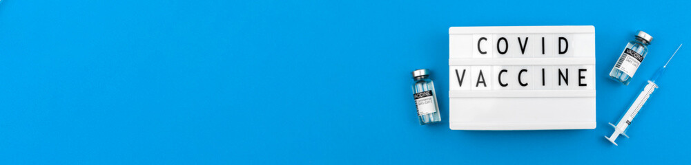 Covid vaccine banner with blue background concept, coronavirus vaccination flat lay photo with vaccine vials and syringe on the table