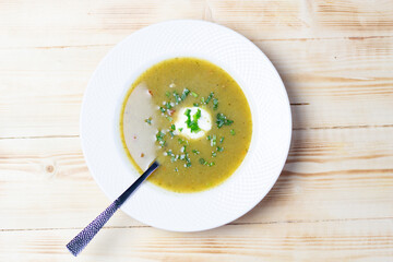 White plate with vegetable cream soup, sour cream, scallion, spoon on wooden background