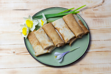 Row of stuffed pancakes laying on green plate  on wooden table with fresh daffodil and crocus flowers