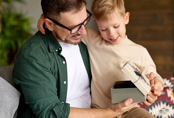 Excited boy son receiving gift box from young loving father on holiday