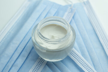 Closeup of a jar of moisturizer and protective face masks. Concept of skin care during the coronavirus pandemic.