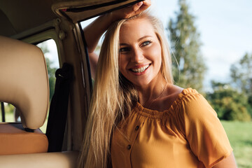 Plakat Beautiful blond woman in casual clothes leaning on camper van looking away