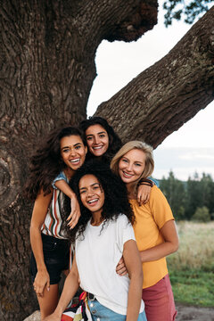 Group of young diverse women standing in front of a big tree and looking at camera