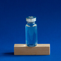 Glass vaccine bottle stands on a wooden cube.