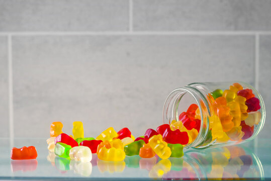 multi colored chewing candies scattered from  a glass can on a gray background