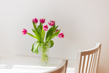 Beautiful brindle tulips with green leaves in a vase on the table. Nice bouquet in a vase on a white table.